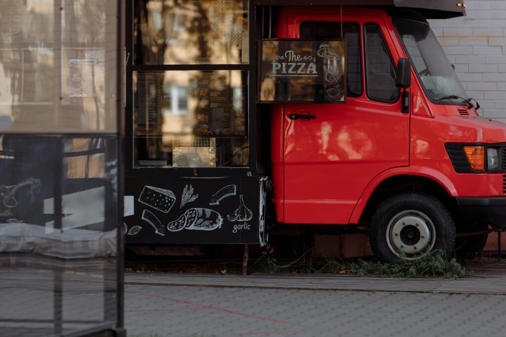 A vibrant red food truck serves delicious pizza in an urban setting, featuring creative menu signage.