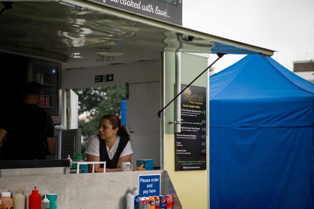 A food truck with staff serving at an outdoor festival with colorful tents.
